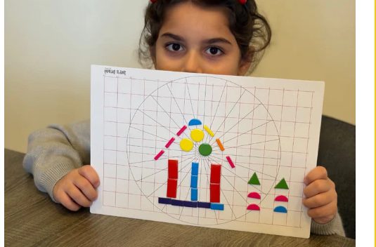 A child holds up a Magic Board with a house built from magnetic shapes